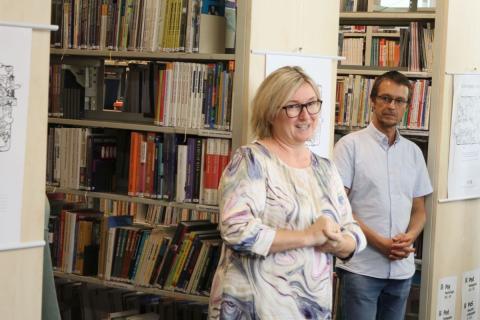 Proslov ředitleky Jaboku Hanky Pazlarové žena stojící před knihovním regálem s vystaveným obrázek a hovoří k ostatním návštěvníkům