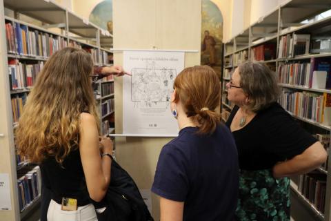 Hledáme slovní spojení Tři zaujaté a zamyšlené ženy stojí před obrázkem s nadpisem Slovní spojení s lidským tělem