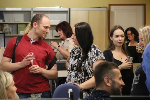 Květa Hošková v rozhovoru s návštěvníkem vernisáže Žena v rozhovoru s mladým mužem, oba jsou obklopeni dalšími lidmi v knihovně