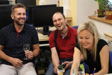 Návštěvníci vernisáže v družné zábavě Skupina dvou mužů a jedné ženy sedí u stolu a smějí se