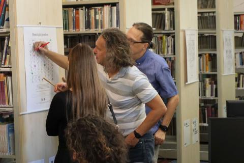 Interakce návštěvníků s obrázky žena a dva muži stojí před obrázekm nadepsaném Pomáhající profes, jeden z mužů vybarvuje část obrázku.